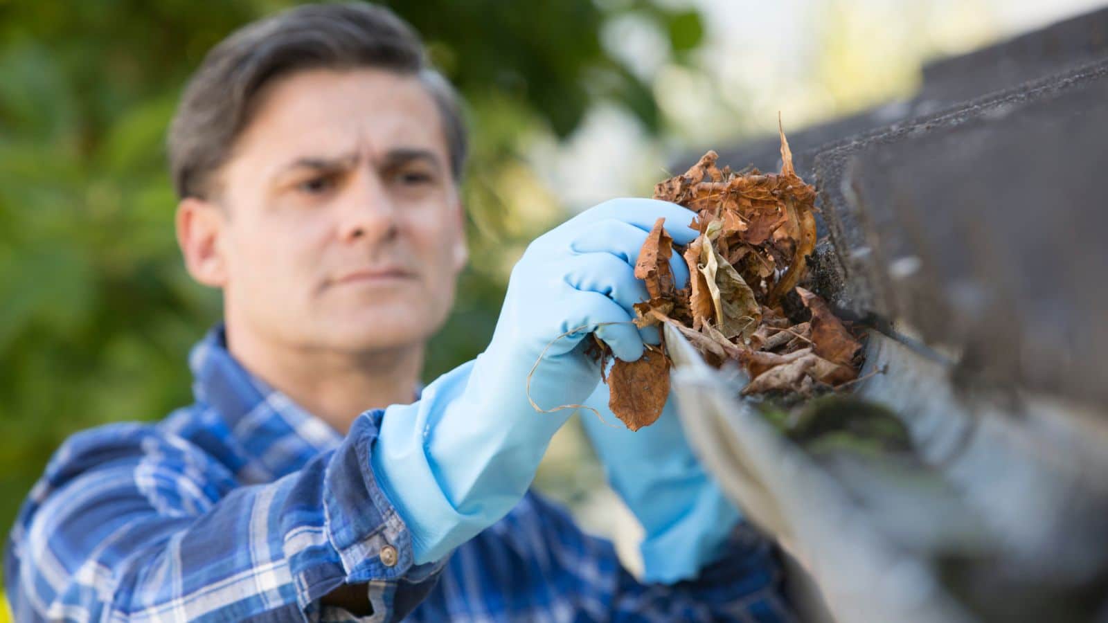 man clears rain gutter for spring maintenance