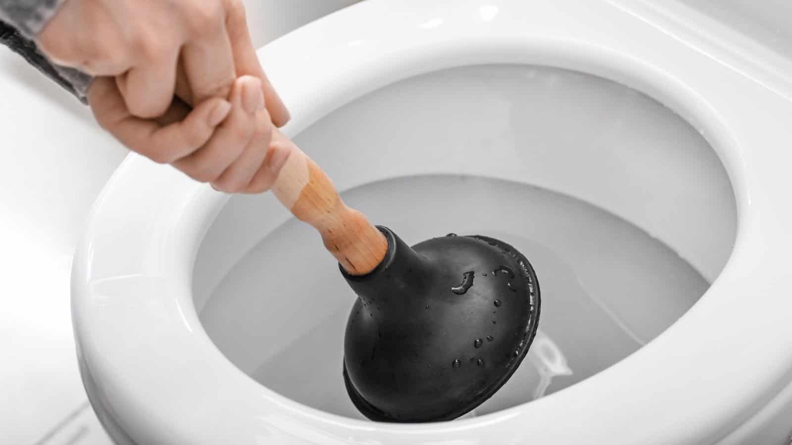 Young woman using plunger to unclog a toilet bowl