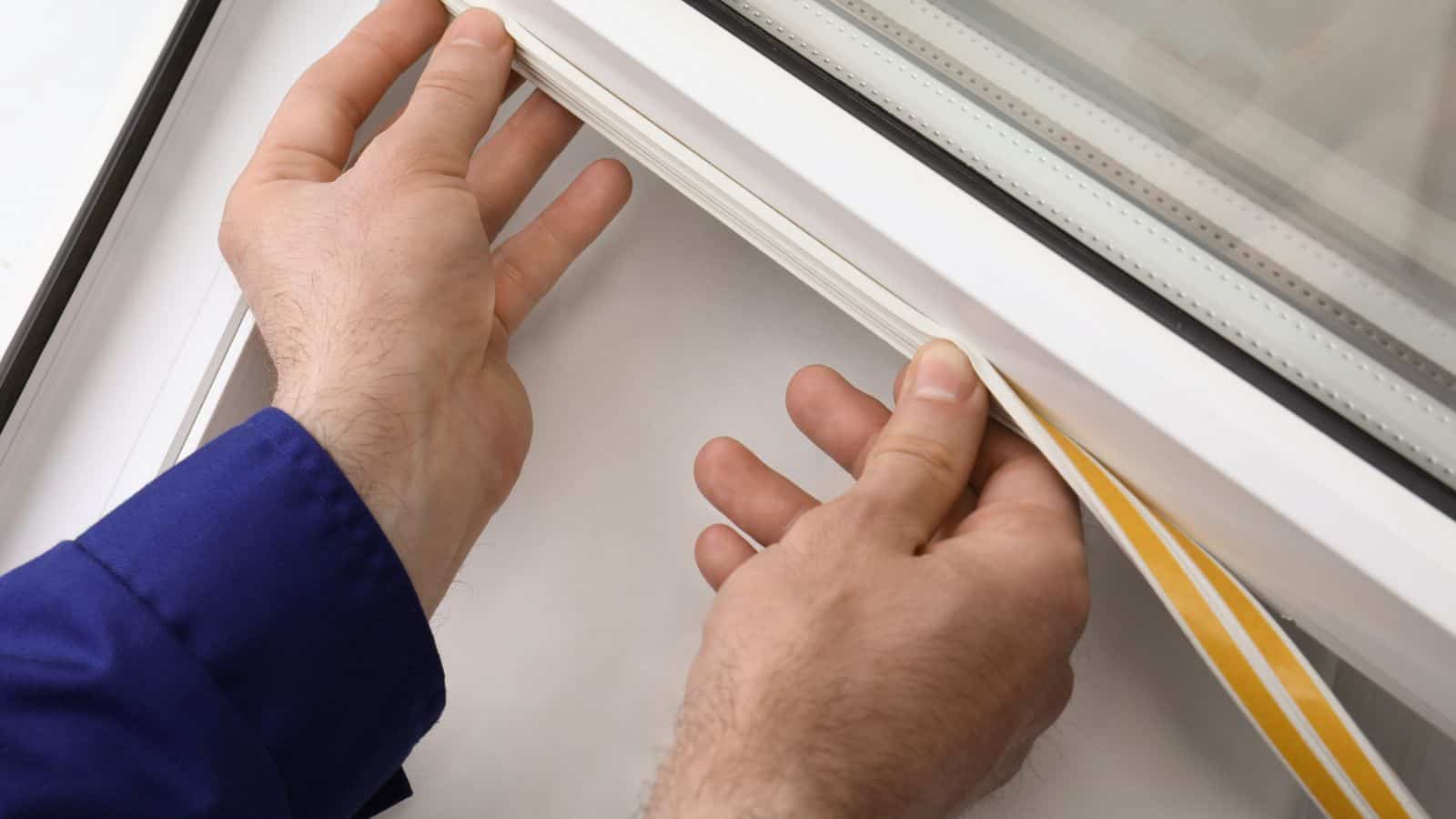 Worker putting rubber draught strip onto window indoors