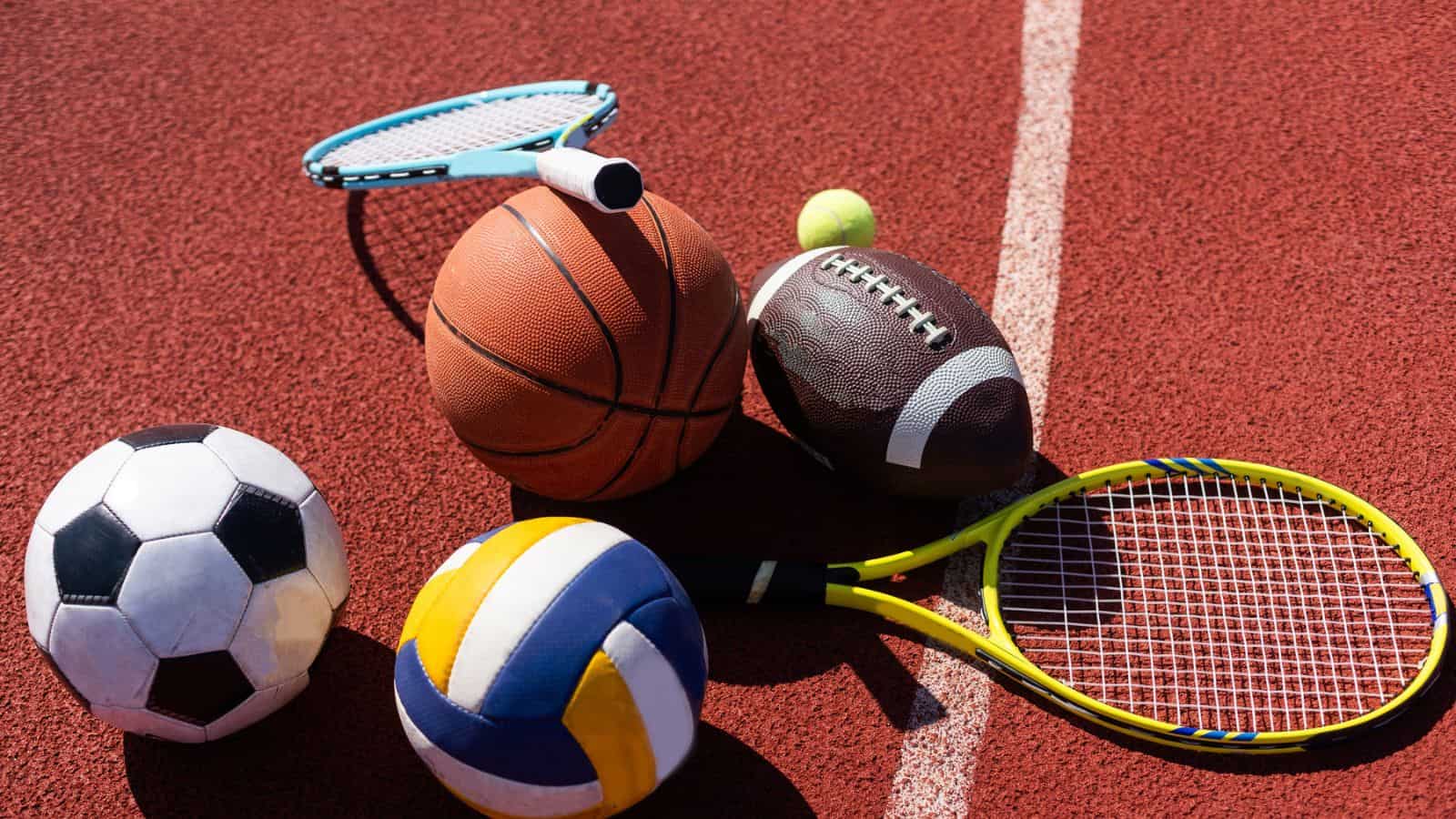 A variety of sports equipment including an american football, a soccer ball, a tennis racket, a tennis ball, and a basketball