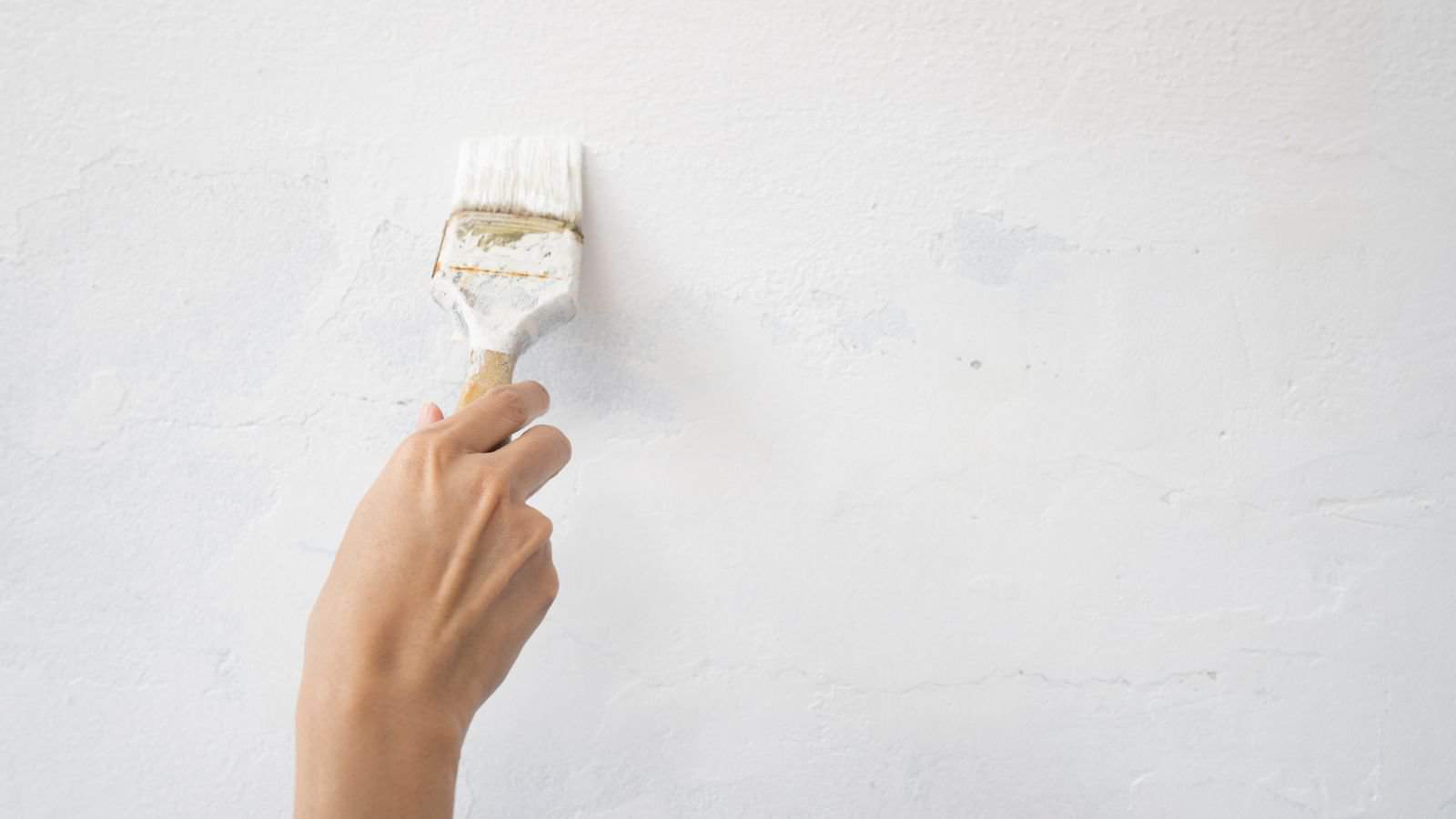 Hand worker holding brush painting white on the wall house
